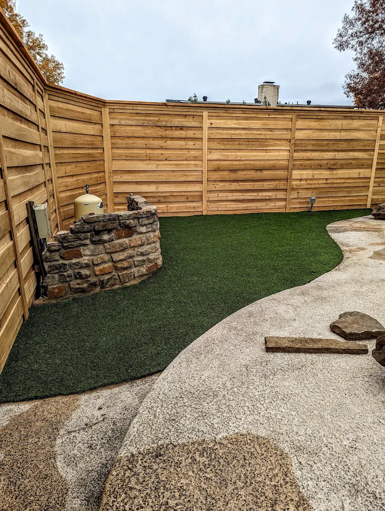 Synthetic turf side yard with a horizontal wood fence and a stacked stone planter
