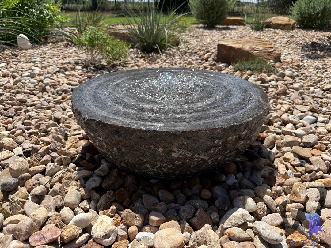 Stone fountain bowl installed in a gravel basin
