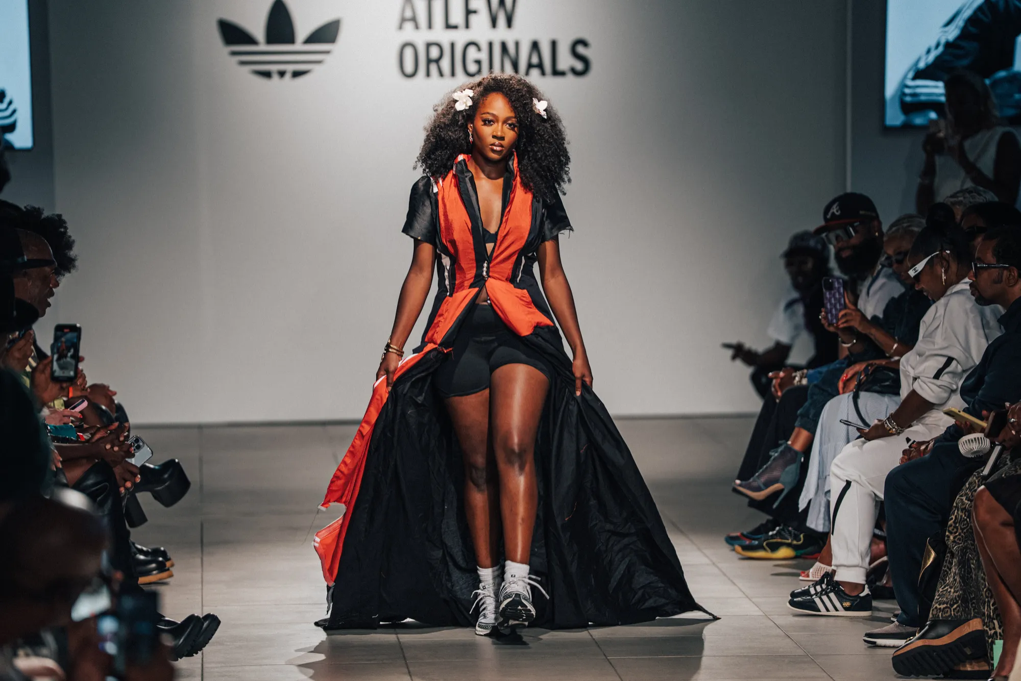 A model in a red and black gown walks the ATLFW Originals runway between rows of guests