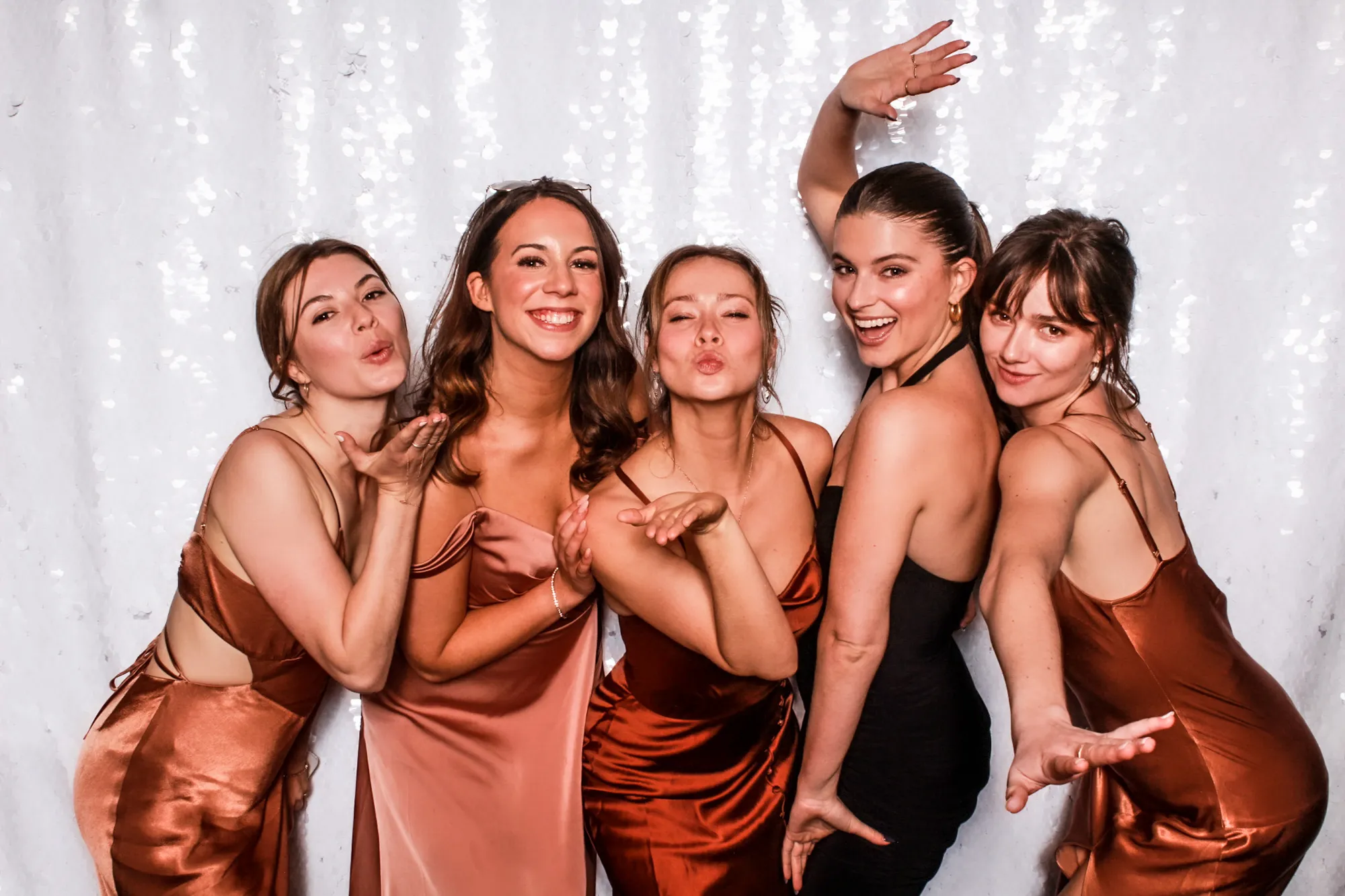 Friends in satin gowns laughing and blowing kisses at the photo booth