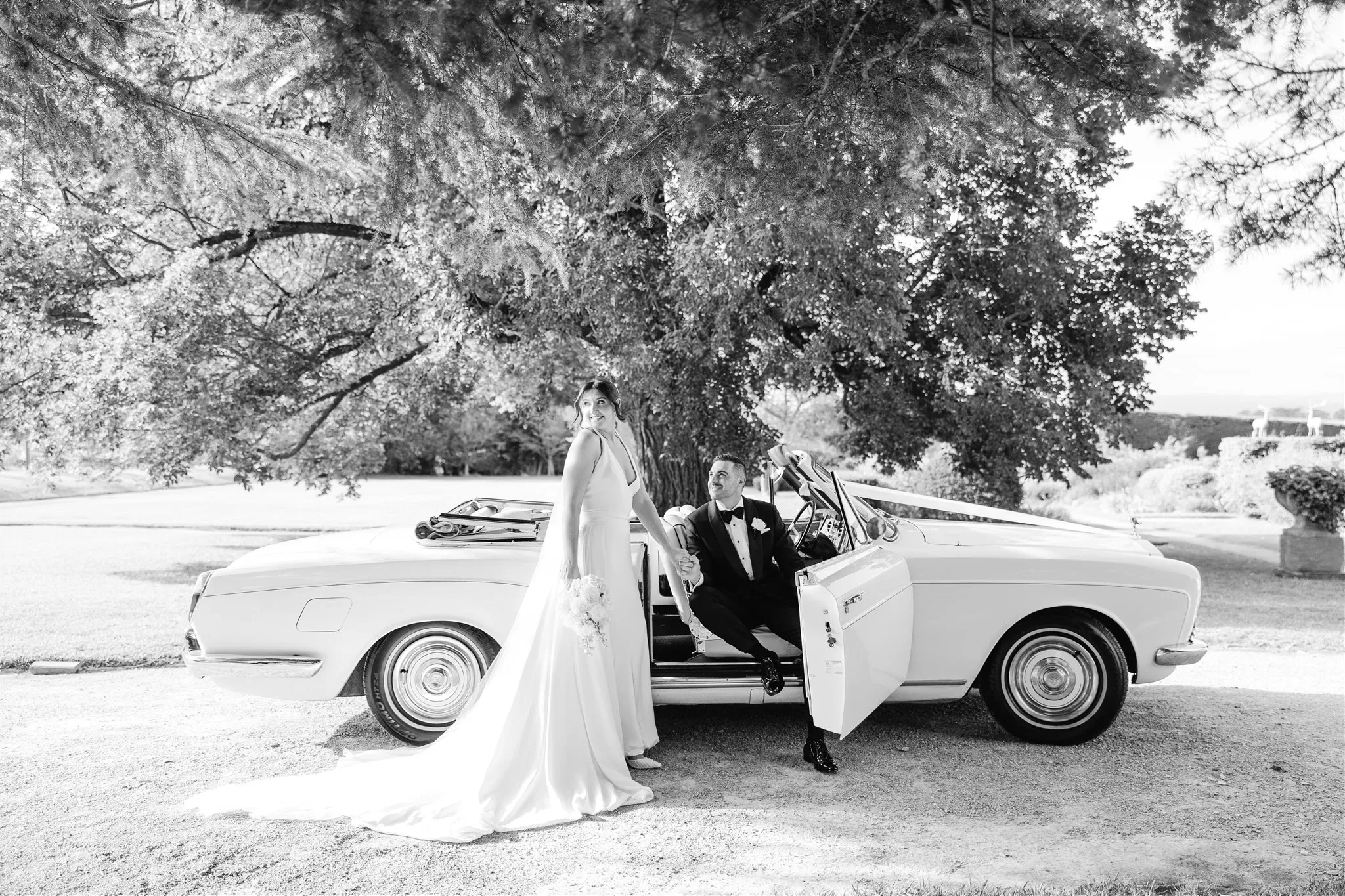 Bride and groom beside a vintage car under a wide tree