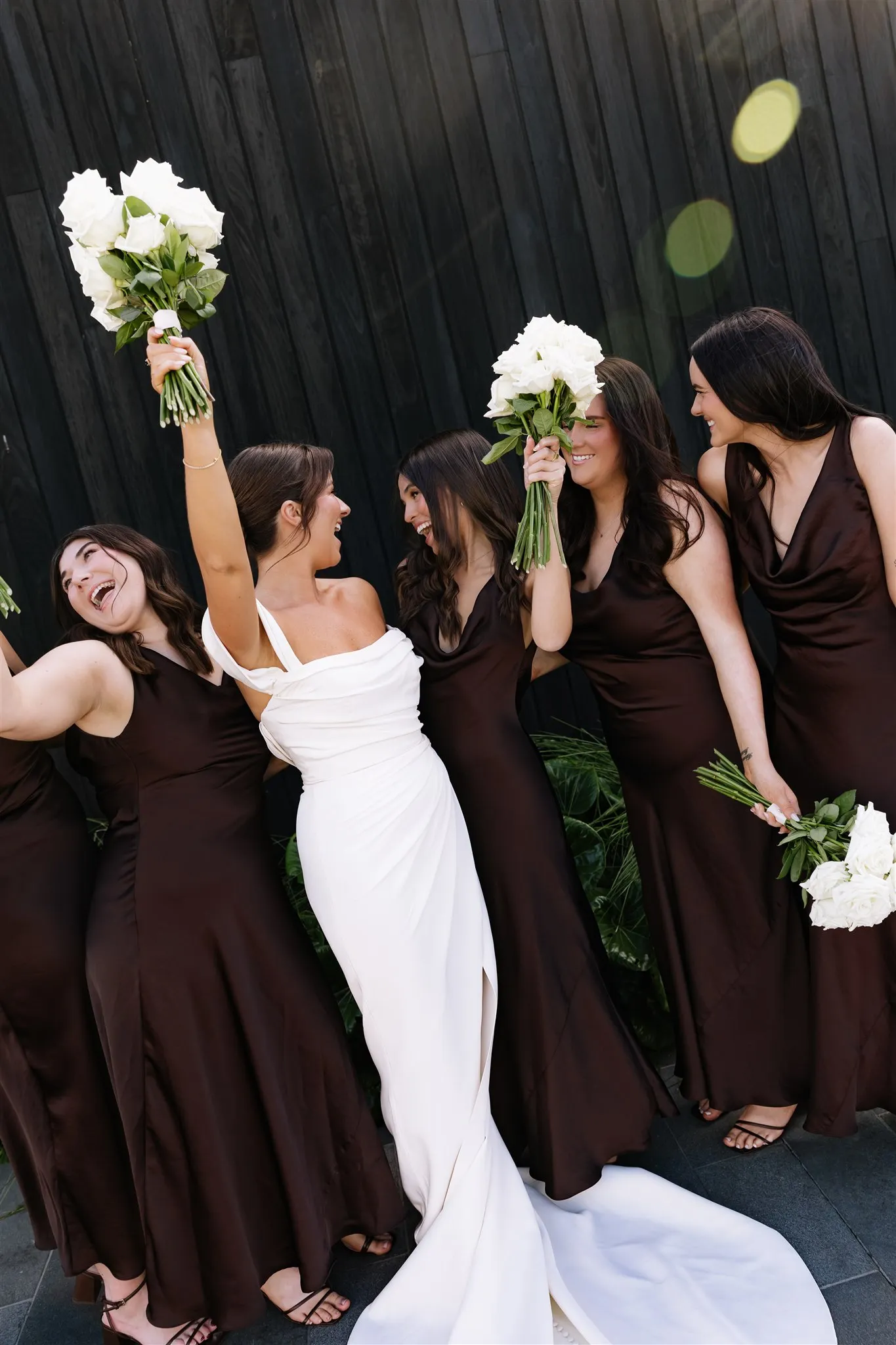 Bridesmaids in chocolate satin lifting their bouquets