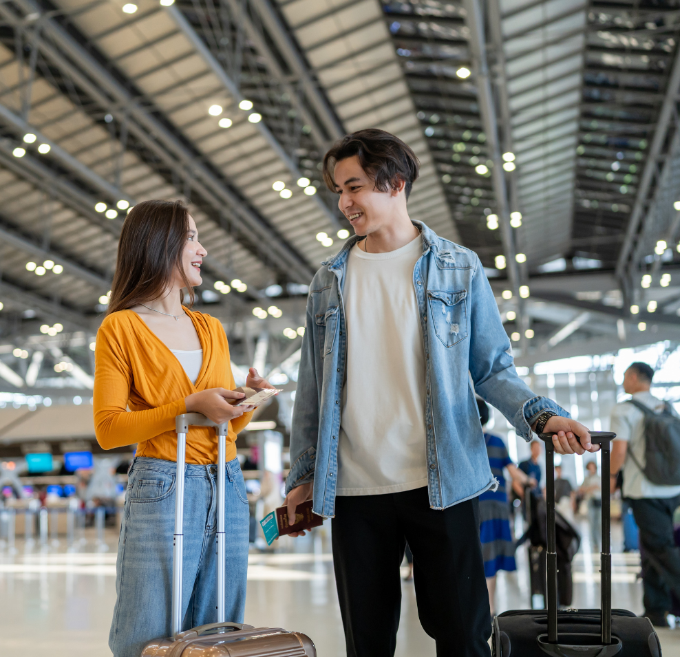 Pareja de viajeros con maletas en un aeropuerto, aprovechando la temporada "hombro" para viajar más barato.