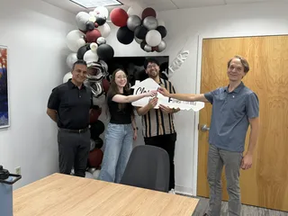 Four people celebrating with a large Closed key and balloons.