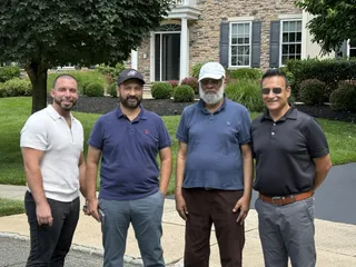 Four people gathered outside a stone-front home.
