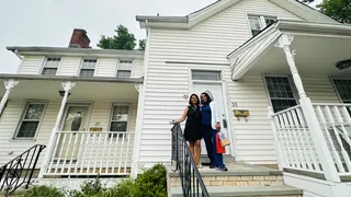 Two people standing outside a white home.