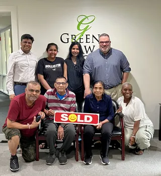 A group posing with a Sold sign.