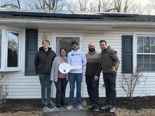 Five people celebrating with a Sold sign outside a home.