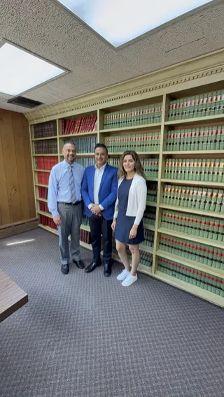 Paul Singh in a blue jacket with two people in front of bookshelves.