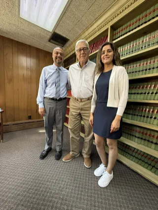 Three people posing together in a room lined with bookshelves.