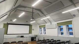 Ceiling panels, a projector and a screen above rows of chairs at the Old Girls School Community Centre.