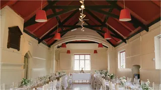 Wedding tables beneath the red ceiling and dark timber roof trusses at Hambleden Village Hall.