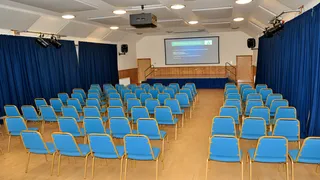 Rows of blue chairs face a projection screen beneath ceiling panels at Tullynessle and Forbes Public Hall.