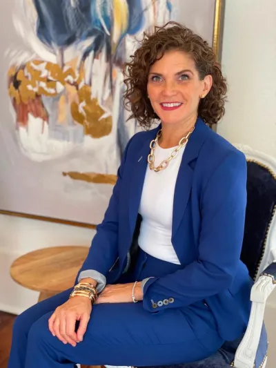 Bridget Truxillo in a blue suit, seated in front of an abstract painting