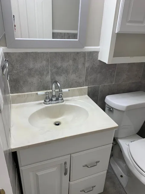 White vanity and toilet with gray tile in a bathroom cleaned by Pretty in Pink Cleaning Service in Wetumpka, AL