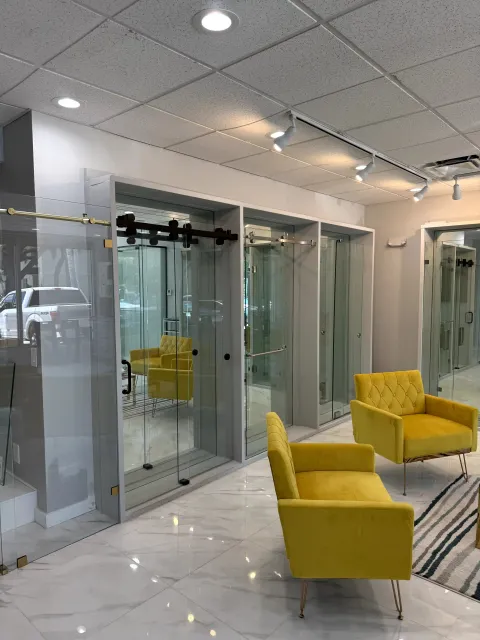 Glass shower displays with different sliding hardware finishes beside yellow chairs