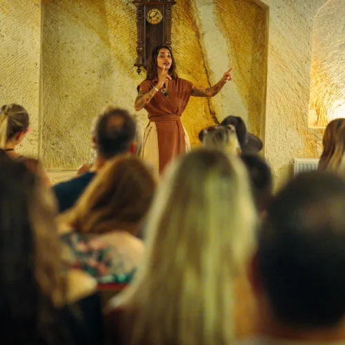 A speaker addressing a seated audience in a cave