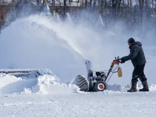 Person clearing a snowy driveway with a snow blower
