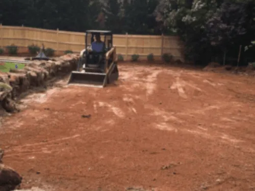 Compact track loader grading bare soil in a fenced backyard