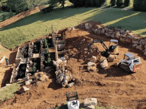 Boulder retaining walls being built on a sloped yard with compact loaders