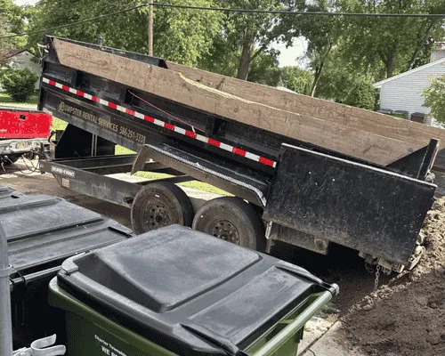 Dump trailer loaded with dirt and debris next to green trash carts