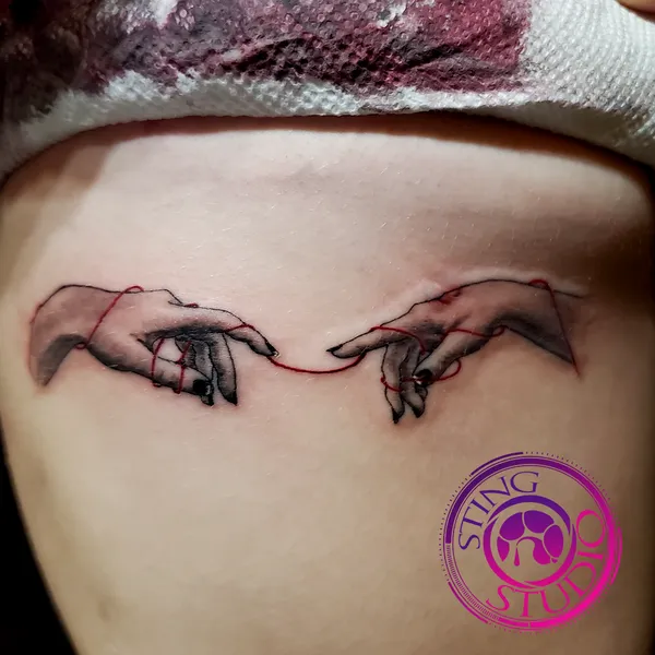 Red ribbon fingers pointing tattoo by Derrick at Sting Studio Ottawa