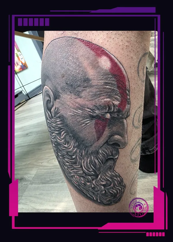 Black and grey realism portrait of Kratos with his red war-paint accent on the calf, fresh tattoo by Sting Studio Ottawa