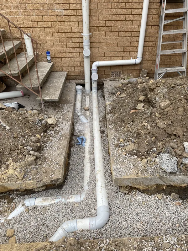New sewer pipework and inspection openings laid in gravel beside a brick building