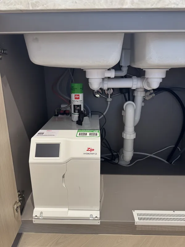 Instant hot water unit installed under a sink with pipework