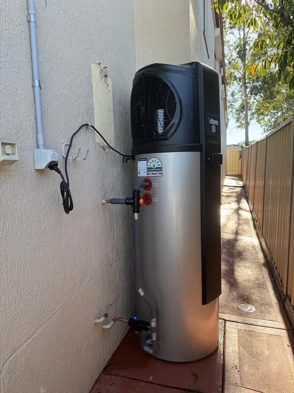 Heat pump hot water unit installed against a wall with copper pipework and valves