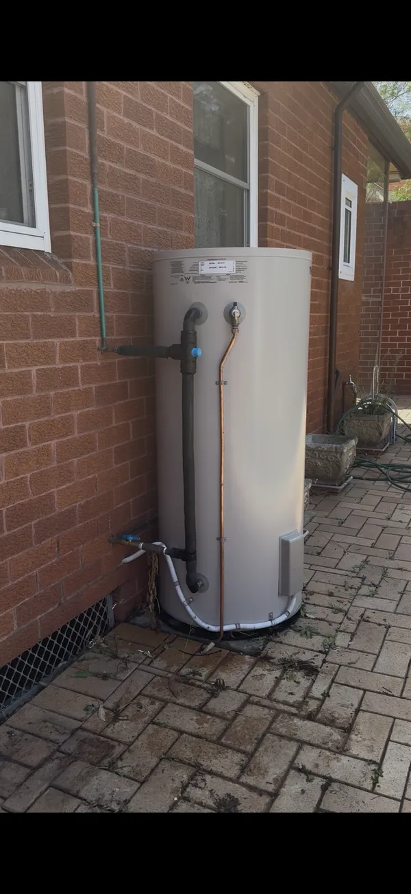 Electric storage hot water tank installed against a brick wall with copper pipework