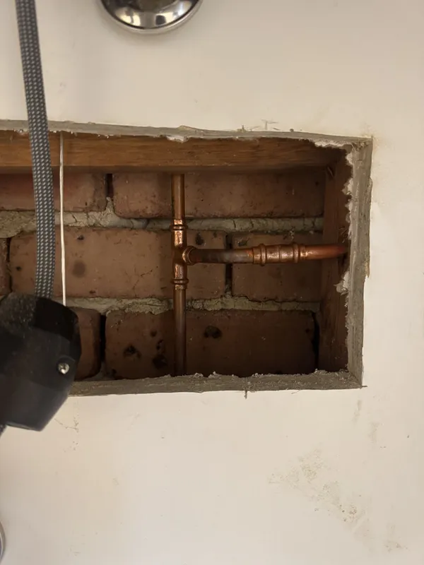 Opened wall cavity exposing copper pipework and a valve against brickwork