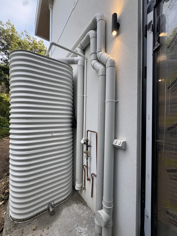 Corrugated rainwater tank beside a house with downpipes and copper pipework