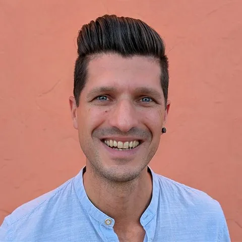Porträt von Frank Kraeh, lachend vor einer orangen Wand