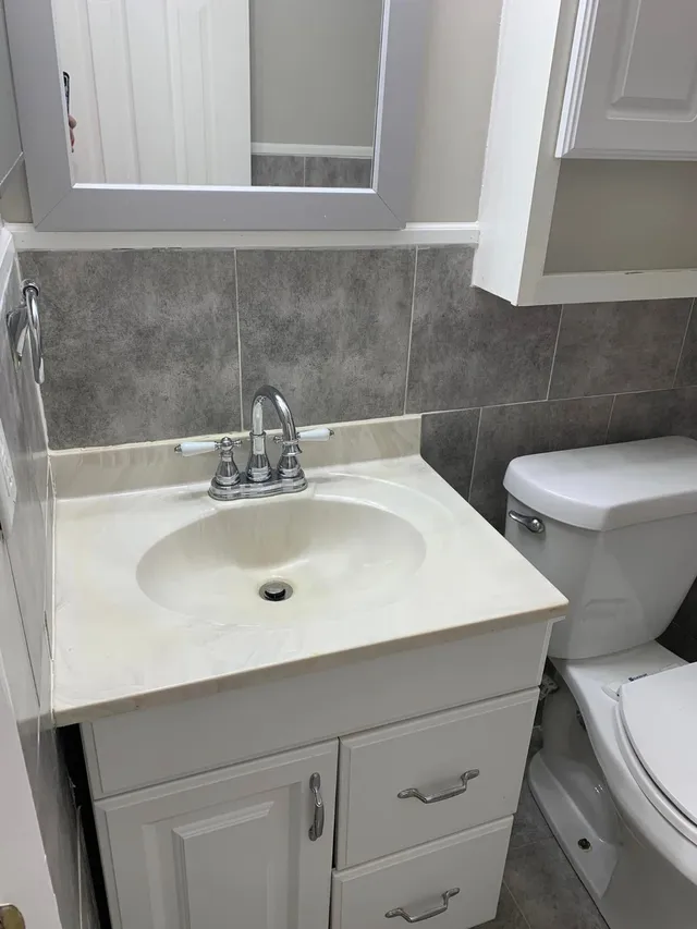 White vanity and toilet with gray tile in a bathroom deep-cleaned by Pretty in Pink Cleaning Service in Wetumpka, AL