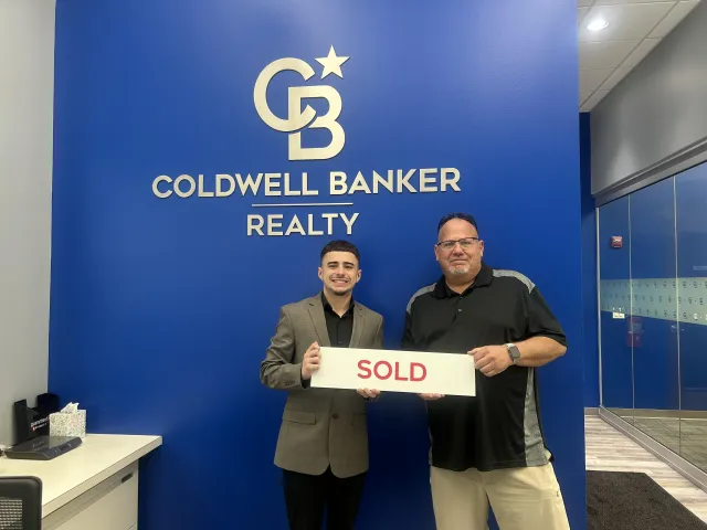 Brenden Gutbrod with clients holding a Sold sign