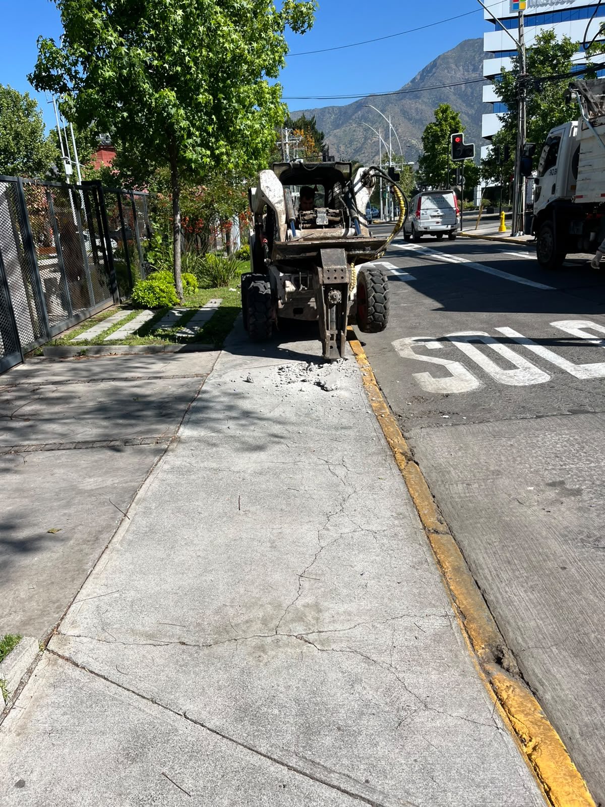 Demolición de vereda con minicargador frente a un edificio comercial