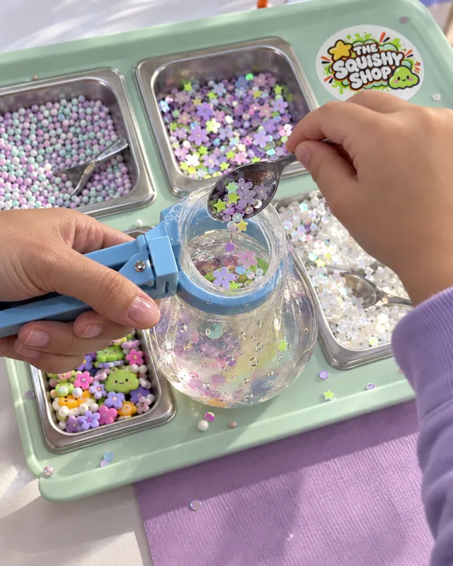 Hands adding pastel confetti to a clear squishy at a mint activity station