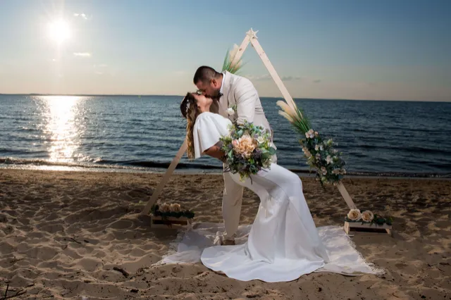 Pareja besándose bajo un arco floral en la playa al atardecer