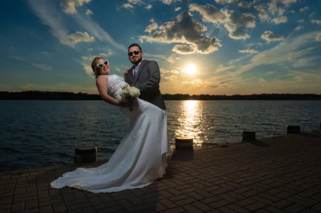 El novio inclina a la novia junto al agua al atardecer