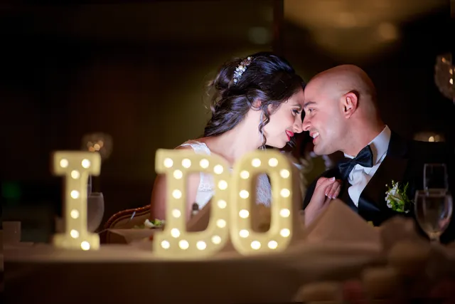 Pareja compartiendo un momento íntimo detrás de letras luminosas I DO