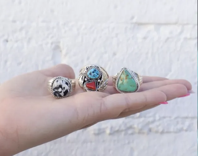 Three handmade sterling silver rings with turquoise and other stones, held in an open hand