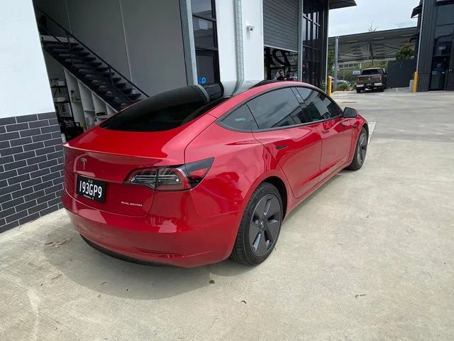 A red tesla model 3 is parked in front of a building - window tinting by Tint Wright Brisbane