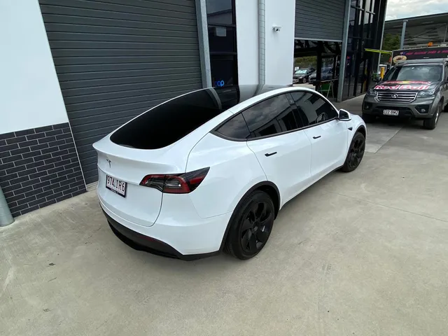 A white tesla model y is parked in front of a building - window tinting by Tint Wright Brisbane