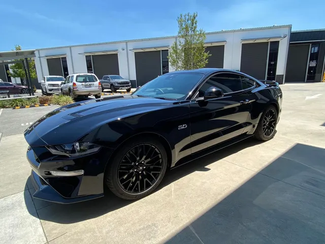 A black ford mustang is parked in a parking lot in front of a building - window tinting by Tint Wright Brisbane