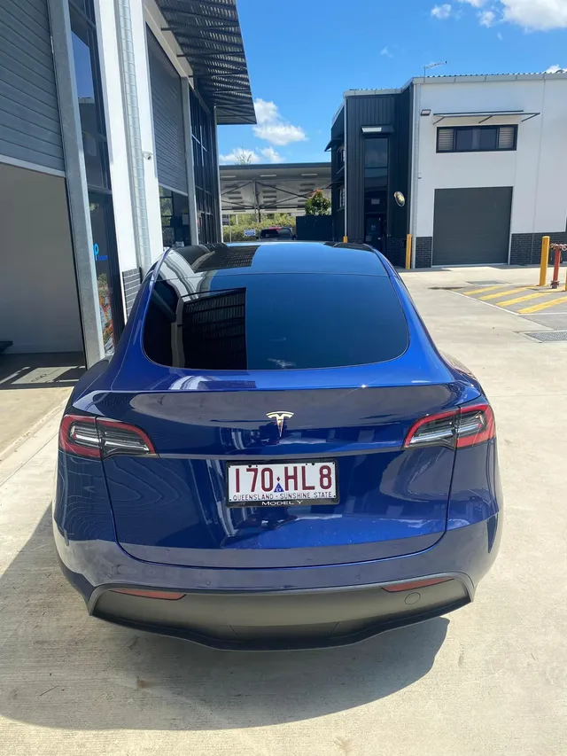A blue tesla model 3 is parked in front of a building - window tinting by Tint Wright Brisbane