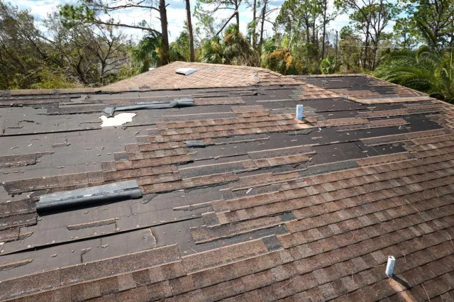 Shingle roof with missing and torn shingles after a storm