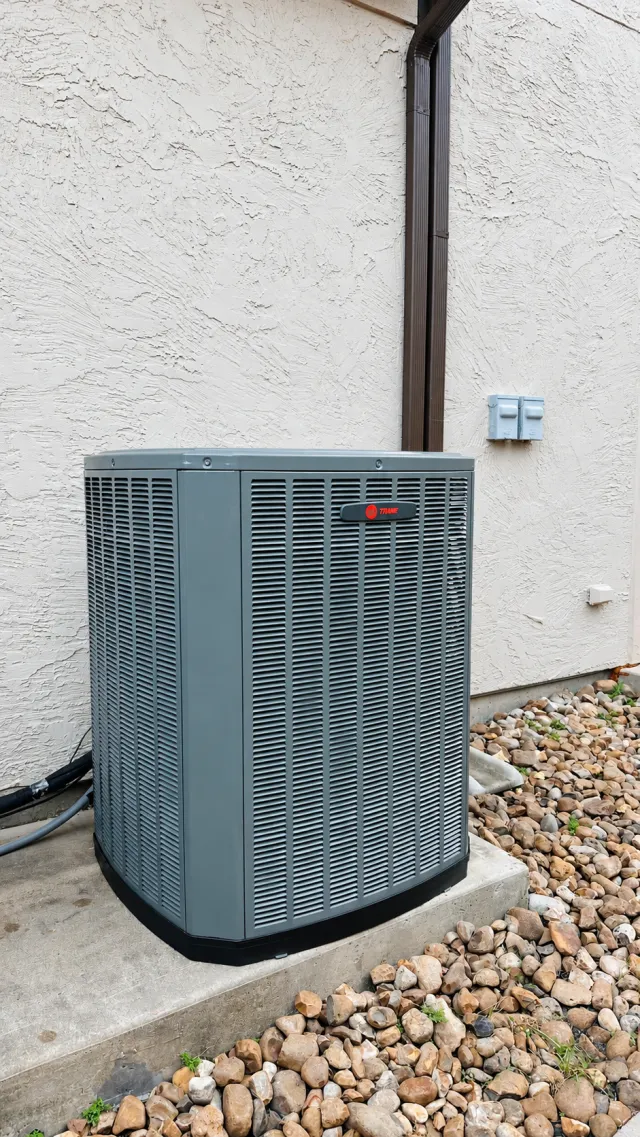Trane air-conditioning condenser beside a white stucco wall