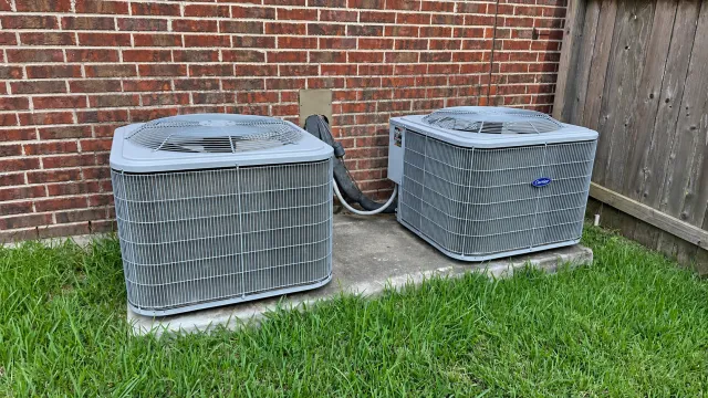 Two Carrier outdoor condensers on a concrete pad beside a brick home