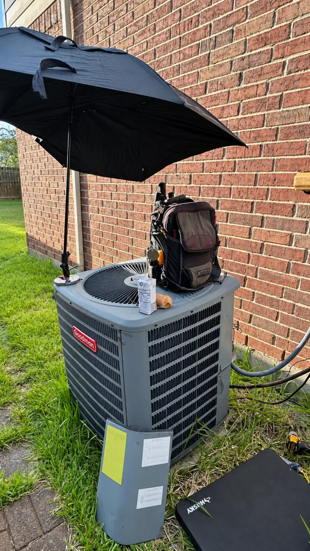Goodman air conditioner during a service visit with tools and a shade umbrella